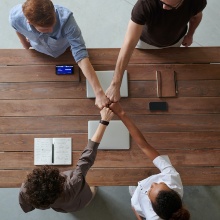 Team of four people at a table fist-bumping
